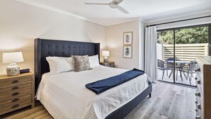 Ein Schlafzimmer mit Bett, Nachttischen, Deckenventilator und Blick auf eine Außenpatio.