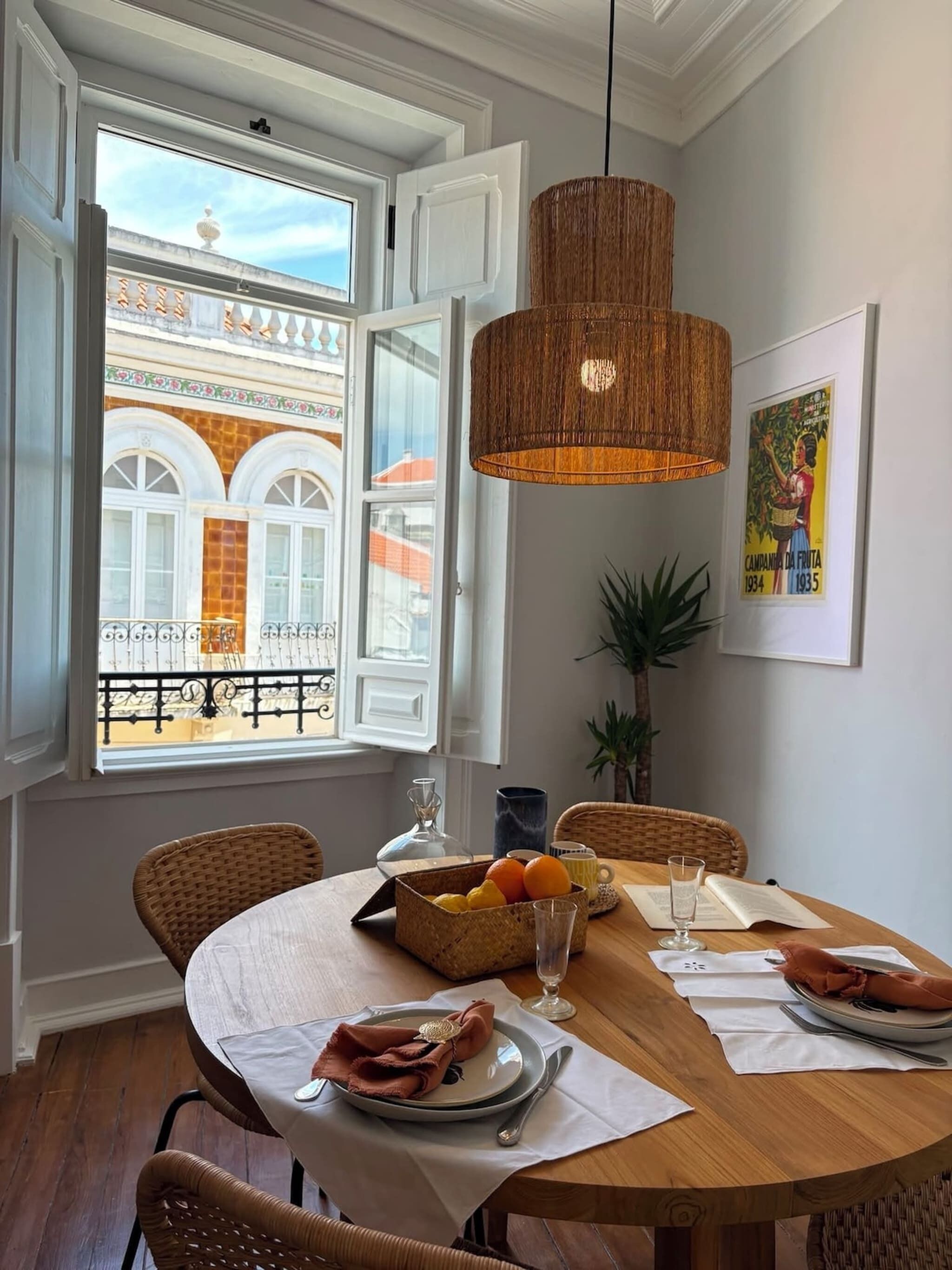 Een eetruimte met een ronde tafel, rieten stoelen, een hanglamp en een raam met een open deur.
