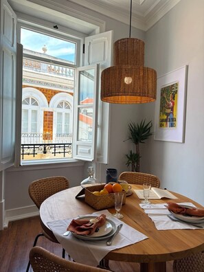 Comedor con una mesa redonda, sillas de mimbre, una lámpara colgante y una ventana con puerta abierta.