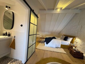 A bedroom with a bed, bedside table, lamp, and a view of the bathroom. - Casa Fataca (Grândola)