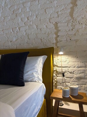 A bed with white and dark pillows, a yellow headboard, and a bedside table with a lamp and two containers. - Casa Fataca (Grândola)