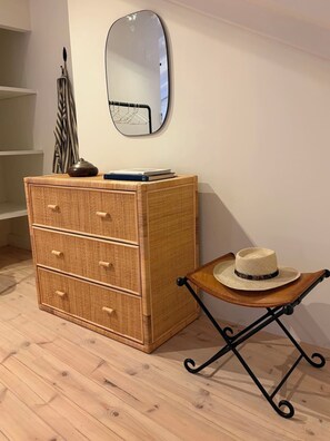 A room with a wicker dresser, a mirror, and a small table with a hat. - Casa Fataca (Grândola)