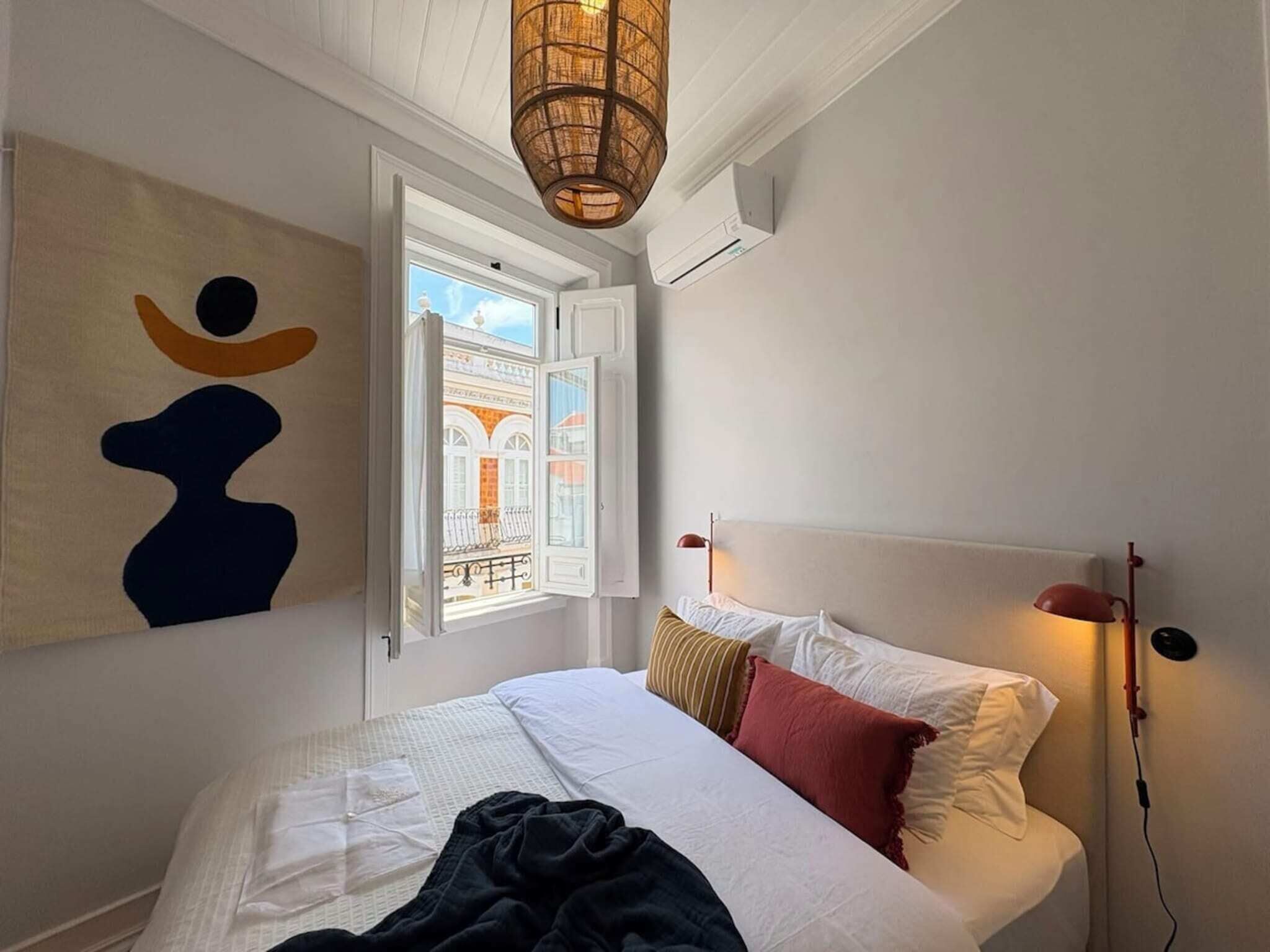 A bedroom with a bed, a window, a wall art piece, and a hanging light fixture.
