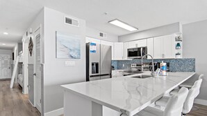 A modern kitchen with white cabinetry, a marble island, and a built-in oven. - Crystal Sands 215a- Saltwater Daze (Destin)