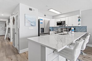 A modern kitchen with white cabinetry, a marble island, and a built-in oven. - Crystal Sands 215a- Saltwater Daze (Destin)