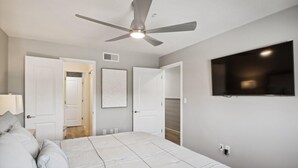 A bedroom with a bed, a ceiling fan, a TV, and white walls. - Crystal Sands 215a- Saltwater Daze (Destin)