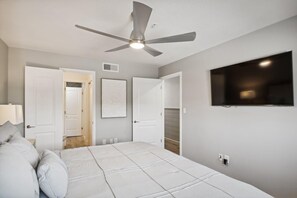A bedroom with a bed, a ceiling fan, a TV, and white walls. - Crystal Sands 215a- Saltwater Daze (Destin)