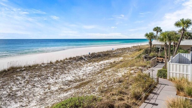 A beach view with a pathway leading to a building with a deck and palm trees. - Crystal Sands 215a- Saltwater Daze (Destin)