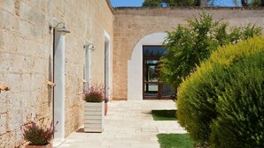 A stone building with a paved walkway, a door, and a small garden area with shrubs. - Masseria Corda di Lana - Suite Deluxe (Leverano)