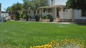 A well-maintained lawn with sprinklers, a building with arched windows, and a variety of plants and flowers. - Masseria Corda di Lana - Suite Deluxe (Leverano)