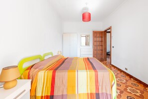 Une chambre à coucher comprenant un lit, une table de chevet, une lampe, un miroir, une armoire et une porte donnant sur une autre pièce.