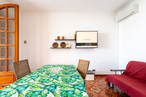 Une pièce comprenant une table à manger, des chaises, un canapé, un téléviseur et une étagère murale décorative.