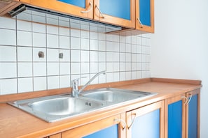 A kitchen with a double stainless steel sink, wooden cabinets, and a tiled backsplash.