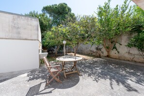 An outdoor patio with a round table and chairs, surrounded by trees and a wall. - Apartment 'Villa Ruggieri - Semiterra' with Private Terrace and Garden (Melendugno)