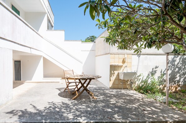 A courtyard with a table and chairs, a white building, and a tree.