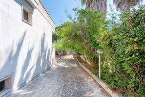A narrow alleyway with a white building on the left, a lamp post on the right, and dense greenery. - Apartment 'Villa Ruggieri - Semiterra' with Private Terrace and Garden (Melendugno)