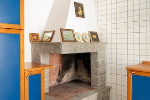 A stone fireplace with framed artwork above it, set in a room with blue cabinetry and a tiled wall.