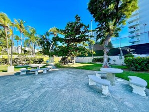An outdoor seating area with benches and tables, surrounded by trees and a building in the background. - Isla Verde Beach/Self Check-in, 1 Parking, Pool (Carolina)