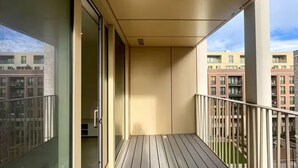 A balcony with a view of adjacent buildings, a glass door, and a wooden floor. - Air conditioner 2 Bedroom central flat (London)