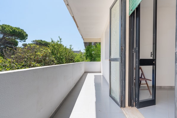 A balcony with a white railing, a glass door, and a view of trees and buildings.