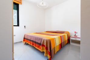 A bedroom with a bed, a nightstand, a lamp, and a window.