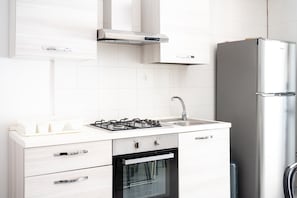 A modern kitchen with white cabinetry, a gas stove, a built-in oven, and a stainless steel refrigerator.
