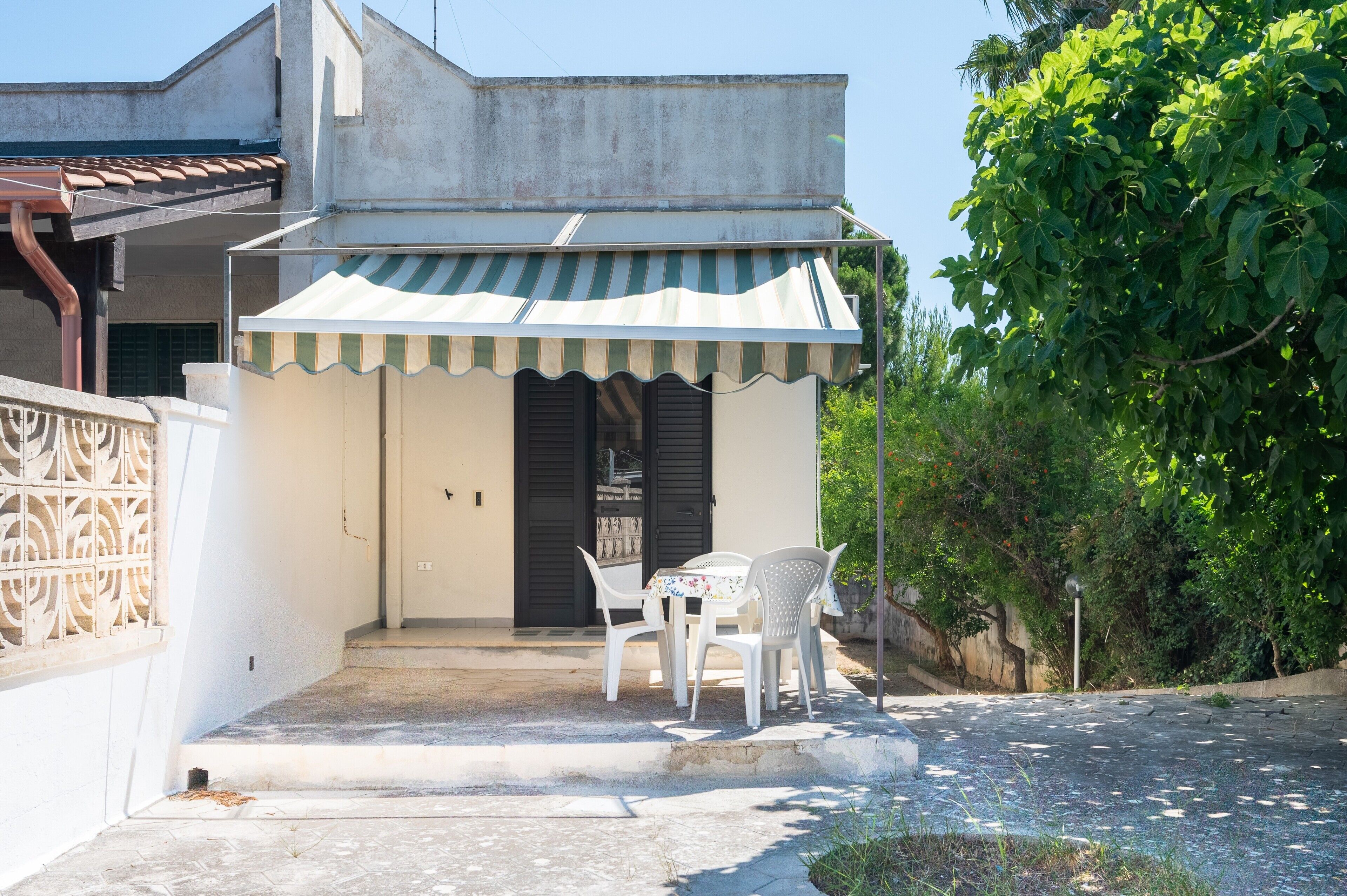 A small building with a striped awning, a door, and a table with chairs outside.