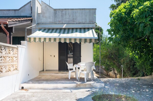 A small building with a striped awning, a door, and a table with chairs outside.