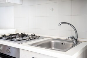 A kitchen with a stainless steel sink, a gas stove, and white tiled walls.