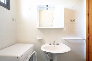 A small bathroom with a washing machine, a sink, and a mirror.