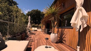 Um deck de madeira com mobiliário de exterior, plantas em vasos e um edifício de madeira com uma janela.