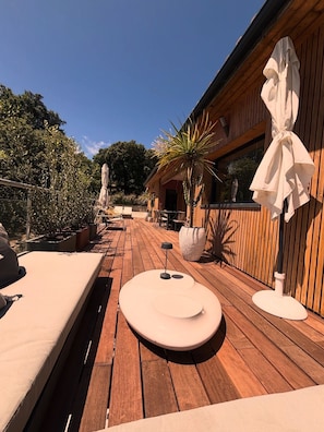 Eine Holzdar Terrasse mit Sitzgelegenheiten, Pflanzkübeln und einem Holzhaus mit Fenster.