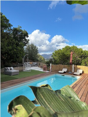 Ein Swimmingpool mit Liegestühlen, einer Sonnenliege und einer Pergola mit Sonnenschirm.