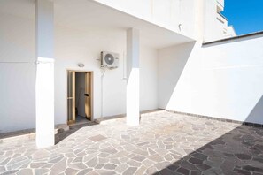 Un bâtiment blanc avec une cour dallée de pierres, une porte et un appareil de climatisation.