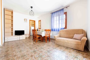Ein Wohnzimmer mit einer Couch, einem Esstisch mit Stühlen, einem Fernseher und einem gemusterten Boden.