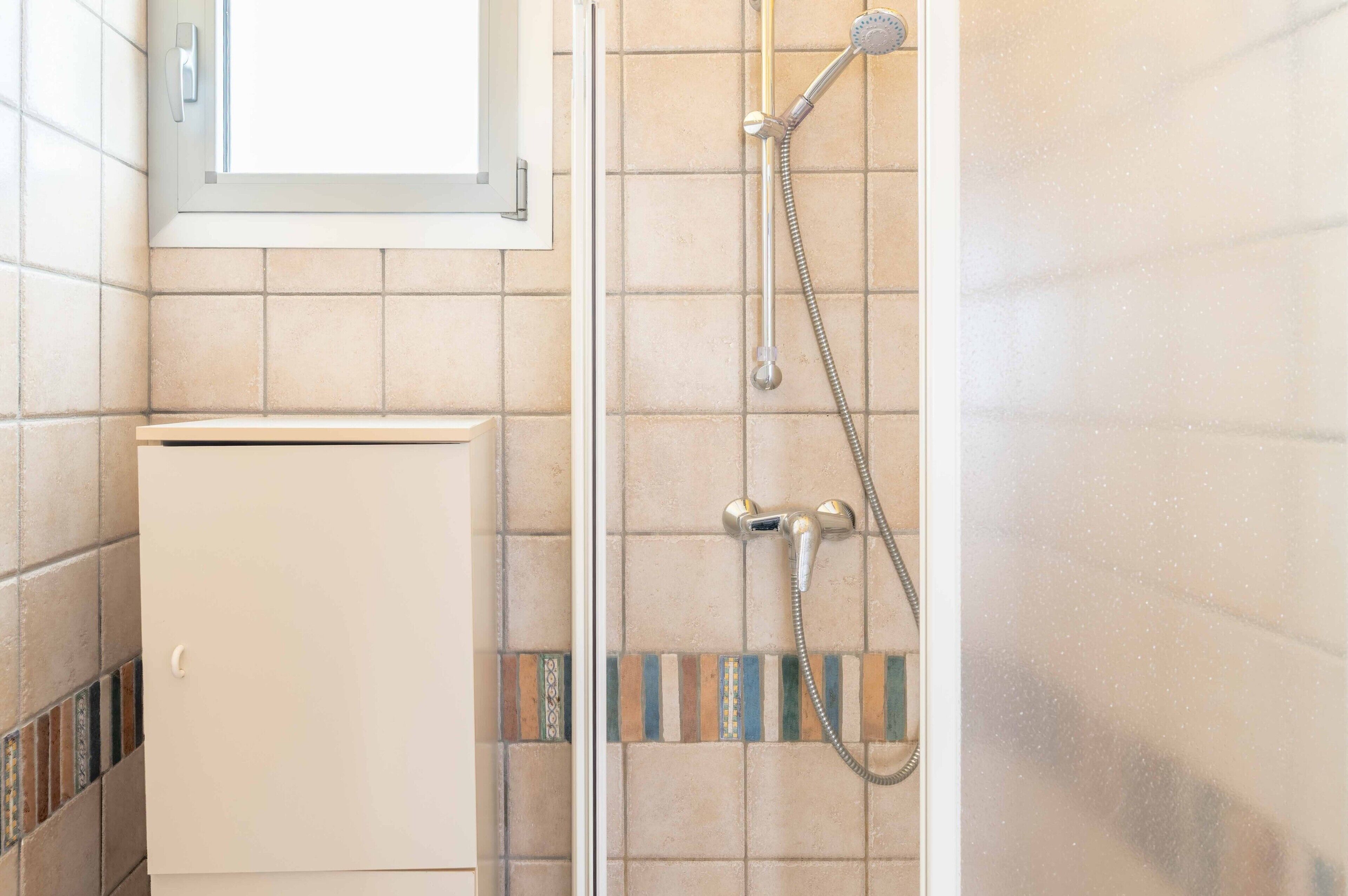 Une douche équipée d’un pommeau de douche à main et d’un robinet mural.
