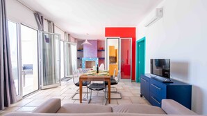 A modern living room with a dining area, a TV, and a kitchen in the background. - Apartment 'Terrazza Sul Mare' with Sea View, Private Terrace and Air Conditioning (San Foca)