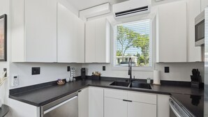 Eine moderne Küche mit weißen Schränken, einer schwarzen Arbeitsplatte, einem Fenster mit Jalousien und einem integrierten Geschirrspüler.