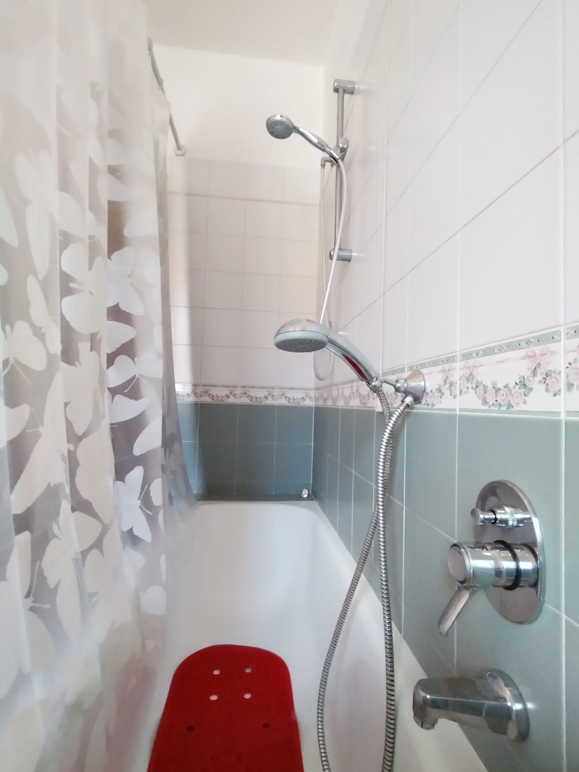 Un baño con ducha, una alfombra de baño roja y paredes de azulejos.