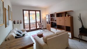 Ein Wohnzimmer mit einer Couch, einem Holztisch, einem Fernsehschrank und einer Glastür zum Balkon.