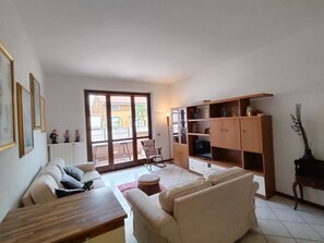 A living room with a sofa, a wooden coffee table, a TV stand, and a sliding glass door leading to a balcony. - Temporary Home Giussano Monza and Brianza (Giussano)