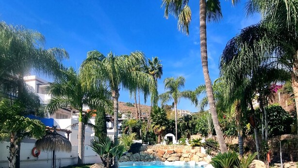 A clear blue pool surrounded by palm trees and a white building. - Oasis Quitapenas Apartment Arroyo Marinos with Pool, Shared Terrace & Wi-Fi (Almuñécar)