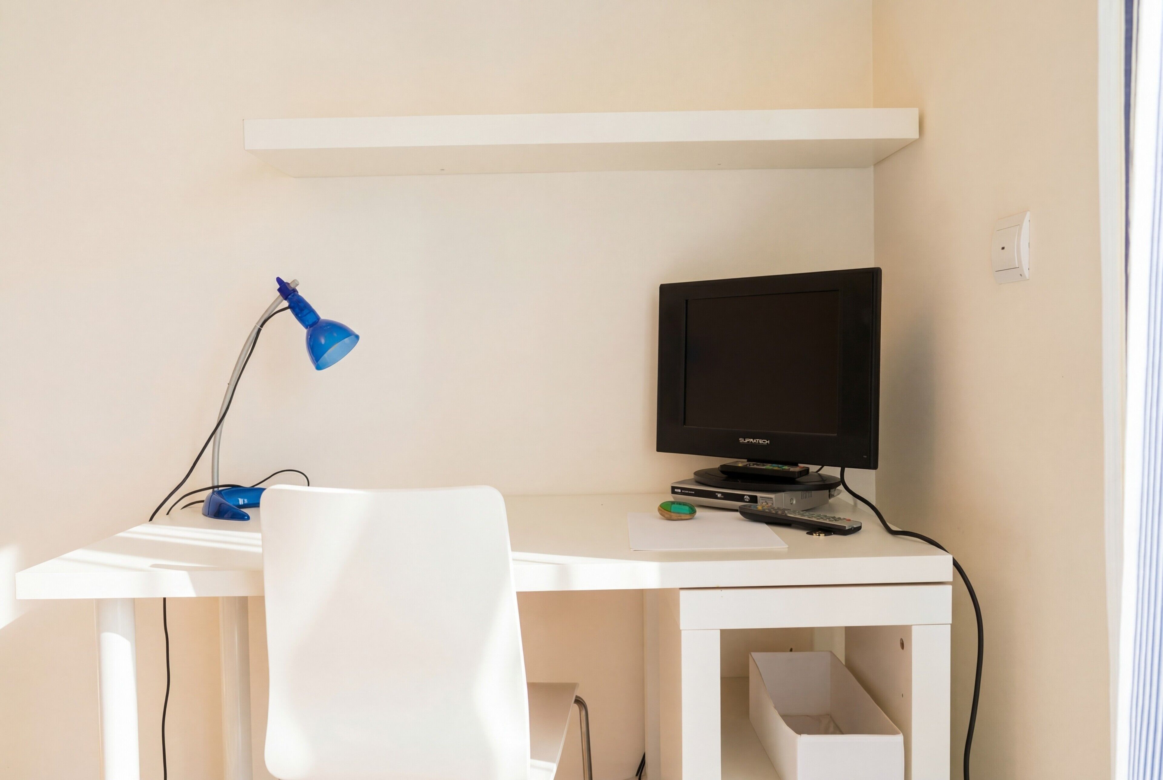 A white desk with a computer monitor, a blue desk lamp, and a white chair.