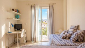A bedroom with a bed, a desk, a chair, a TV, and a balcony with curtains. - Oasis Quitapenas Apartment Arroyo Marinos with Pool, Shared Terrace & Wi-Fi (Almuñécar)