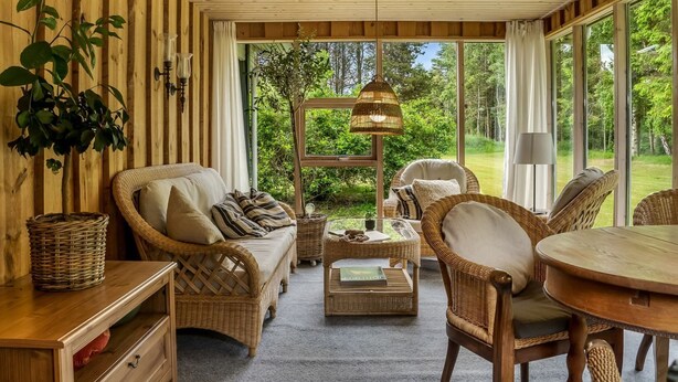 A cozy room with wicker furniture, a wooden ceiling, and large windows offering a view of greenery. - "Linnea" -  from the sea by Interhome (Hals)