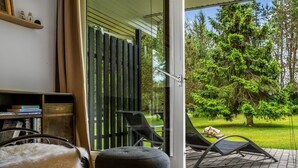 A modern room with a glass door leading to a patio, a black ottoman, a chair, and a bookshelf with books. - "Linnea" -  from the sea by Interhome (Hals)