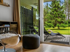 A modern room with a glass door leading to a patio, a black ottoman, a chair, and a bookshelf with books. - "Linnea" -  from the sea by Interhome (Hals)