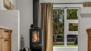 A room with a wood-burning stove, a window with curtains, and a view of greenery outside. - "Linnea" -  from the sea by Interhome (Hals)