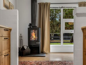A room with a wood-burning stove, a window with curtains, and a view of greenery outside. - "Linnea" -  from the sea by Interhome (Hals)