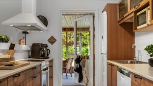 A kitchen with wooden cabinets, a coffee machine, and a view through an open door to a dining area. - "Linnea" -  from the sea by Interhome (Hals)